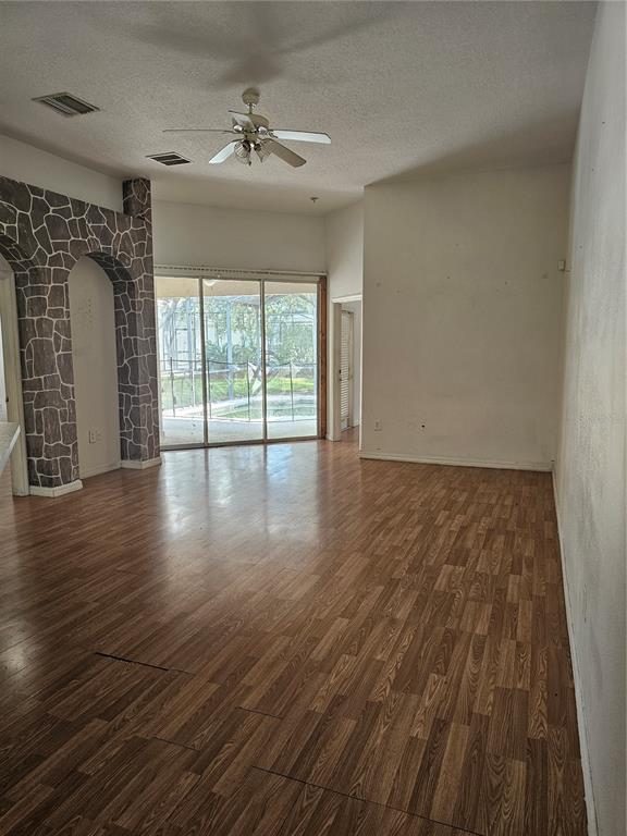 An empty living room features wood-look flooring, a stone-accented archway, and sliding glass doors to a pool — 704 EOLA WAY, HAINES CITY, FL