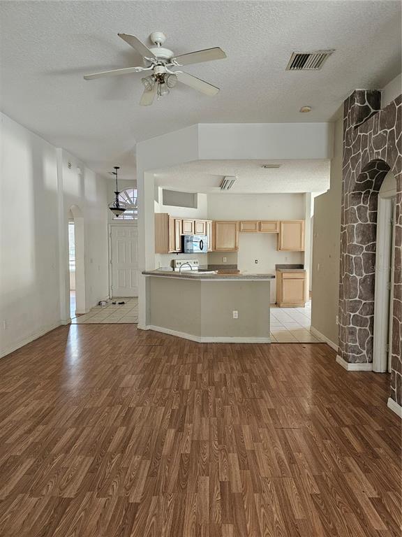 A living room with wood-look flooring leads to an open kitchen with light wood cabinets — 704 EOLA WAY, HAINES CITY, FL