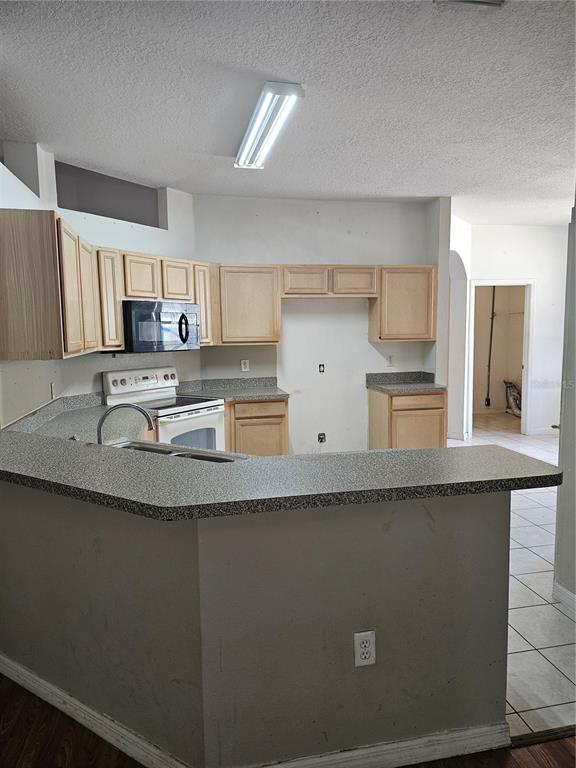 A kitchen features light wood cabinets, speckled laminate countertops, and a peninsula breakfast bar — 704 EOLA WAY, HAINES CITY, FL