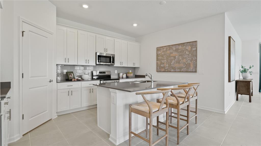 A modern kitchen features white cabinetry, a gray island with bar stools, and stainless appliances — 4286 ST THOMAS WAY, KISSIMMEE, FL