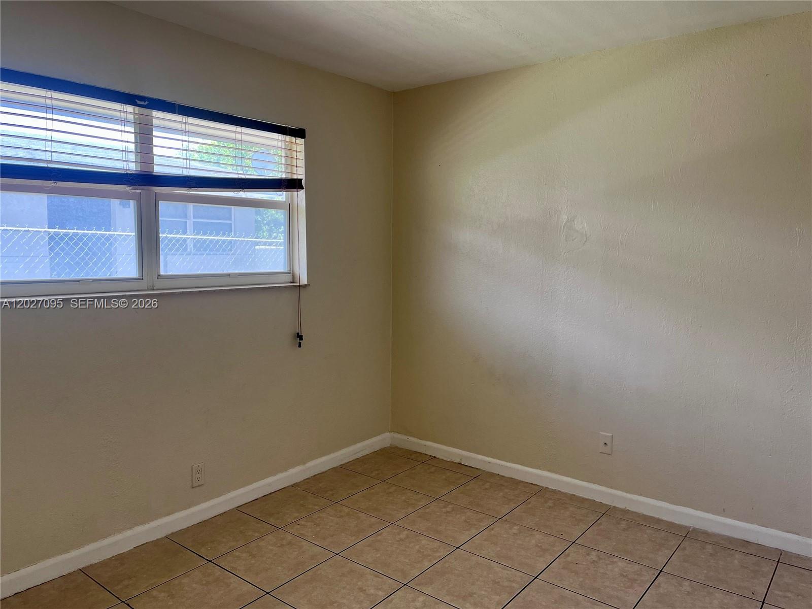 An empty room features beige walls, tile flooring, and a window with horizontal blinds — 109 NW 14th Way # 3, Dania Beach FL 33004, DANIA BEACH, FL