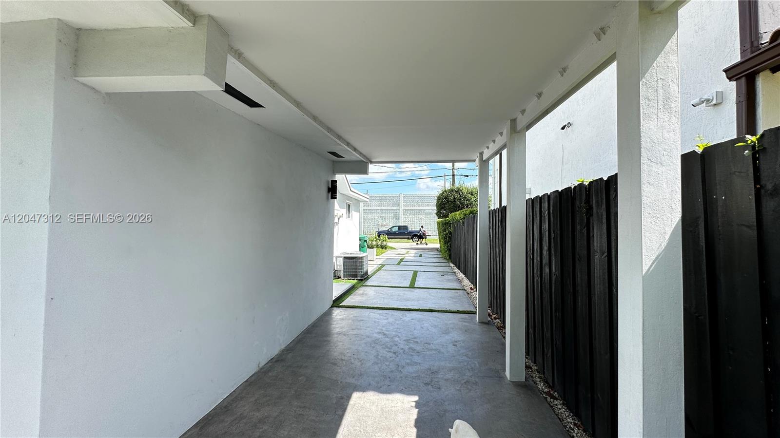 A covered concrete carport leads to a paved driveway with a black wooden fence — 4288 SW 9th St # 1, Miami FL 33134, MIAMI, FL