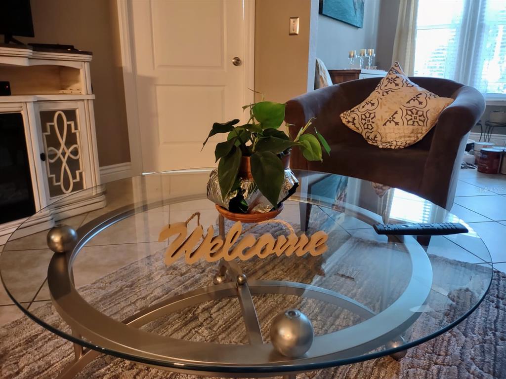 A glass-topped coffee table with a plant and a welcome sign sits in a living room — 2721 VIA MURANO UNIT 311, CLEARWATER, FL