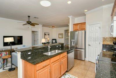 A kitchen with dark granite countertops, wood cabinets, and stainless steel appliances overlooks a living area — 20405 CAVALLO COURT, VENICE, FL