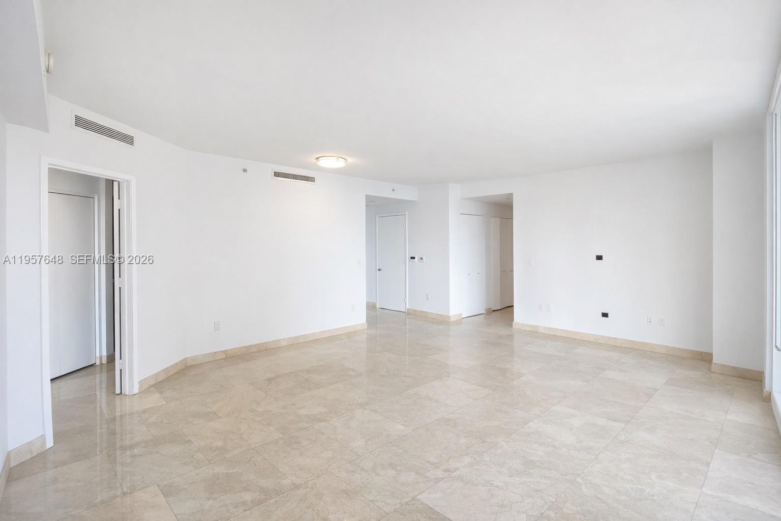 An empty room features white walls, beige tile flooring, and several white interior doors — 901 Brickell Key Blvd # 1603, Miami FL 33131, MIAMI, FL
