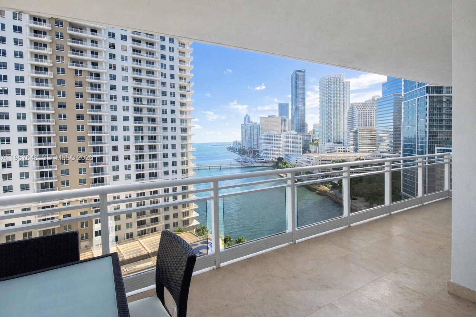 A balcony with a glass railing overlooks a city skyline, a river, and high-rise buildings — 901 Brickell Key Blvd # 1603, Miami FL 33131, MIAMI, FL