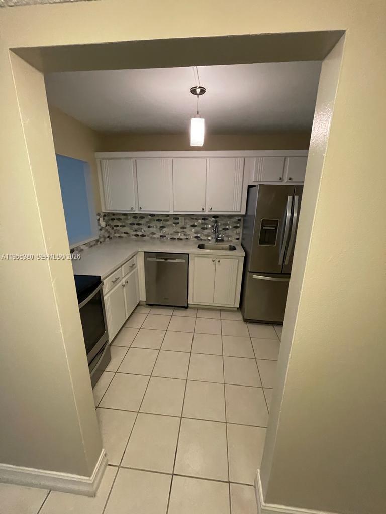 A kitchen features white cabinets, stainless steel appliances, a tiled backsplash, and light floor tiles — 1000 Parkview Dr # 1016, Hallandale Beach FL 33009, HALLANDALE BEACH, FL