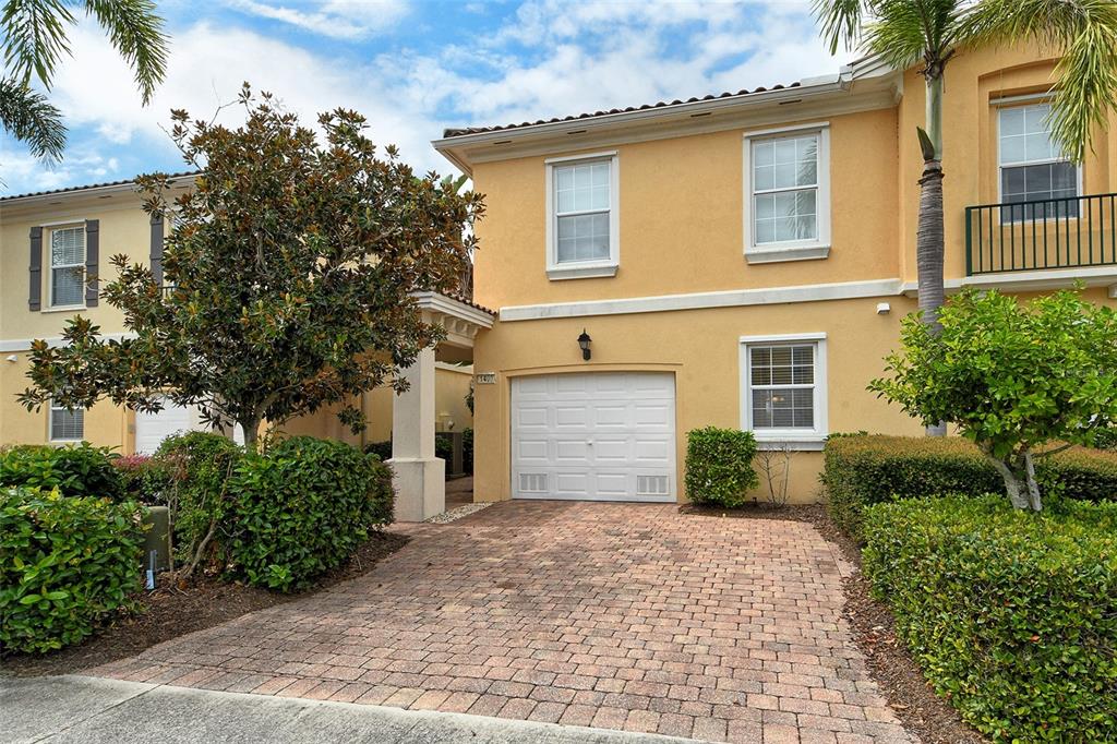 A two-story yellow stucco townhouse with a brick paver driveway and a single-car garage — 1400 BURGOS DRIVE, SARASOTA, FL