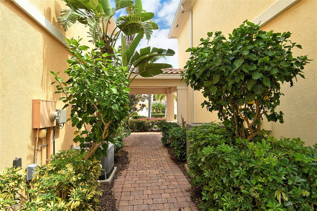 A brick walkway leads through a covered breezeway between two beige buildings with lush landscaping — 1400 BURGOS DRIVE, SARASOTA, FL