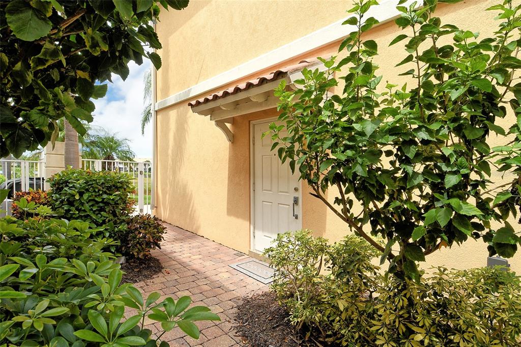 A white door with a small awning is surrounded by lush landscaping and brick pavers — 1400 BURGOS DRIVE, SARASOTA, FL