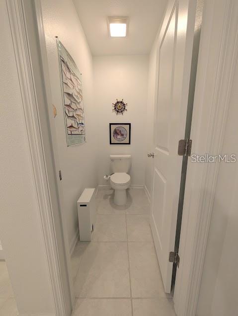 A small, narrow bathroom features a white toilet, light-colored tile flooring, and nautical wall decor — 2860 BIG SUR ROAD, DAVENPORT, FL