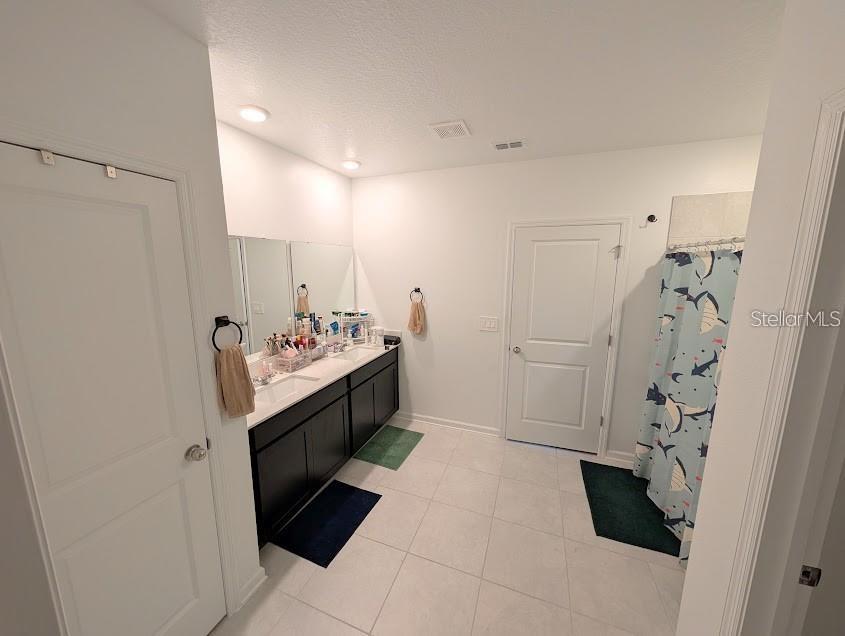 A bathroom features a double vanity with dark cabinets, a tiled floor, and a shower curtain — 2860 BIG SUR ROAD, DAVENPORT, FL