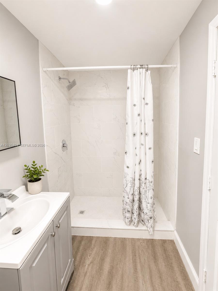 A bathroom features a walk-in shower with marble-look tile, a vanity, and wood-look flooring — 20600 SW 118th Pl, Miami FL 33177, MIAMI, FL