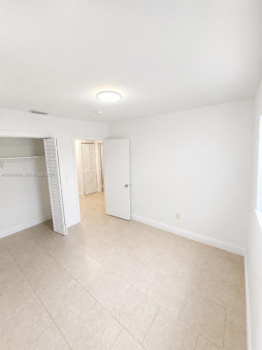 A bedroom with white walls, tile flooring, a closet, and an open doorway — 20600 SW 118th Pl, Miami FL 33177, MIAMI, FL