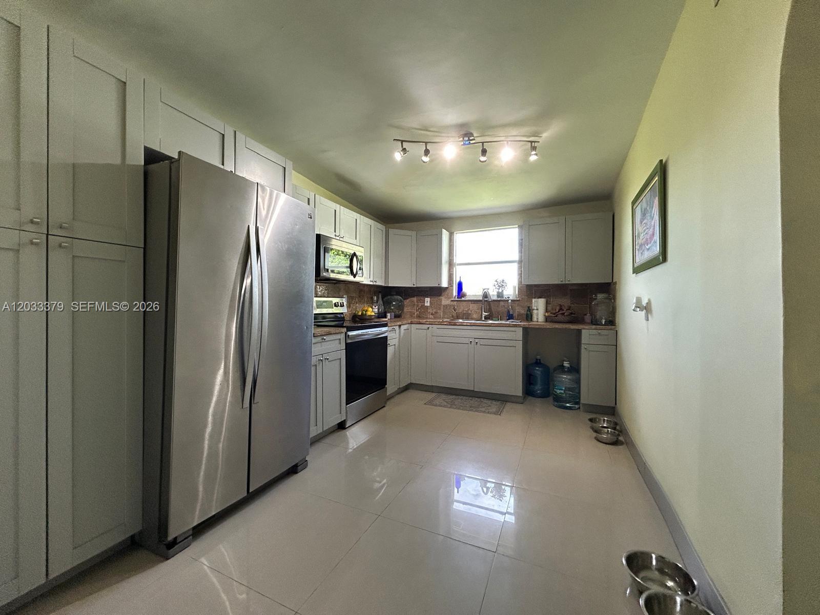 A kitchen features light gray cabinetry, stainless steel appliances, and beige tile flooring — 12098 SW 197th Ave, Miami FL 33196, MIAMI, FL