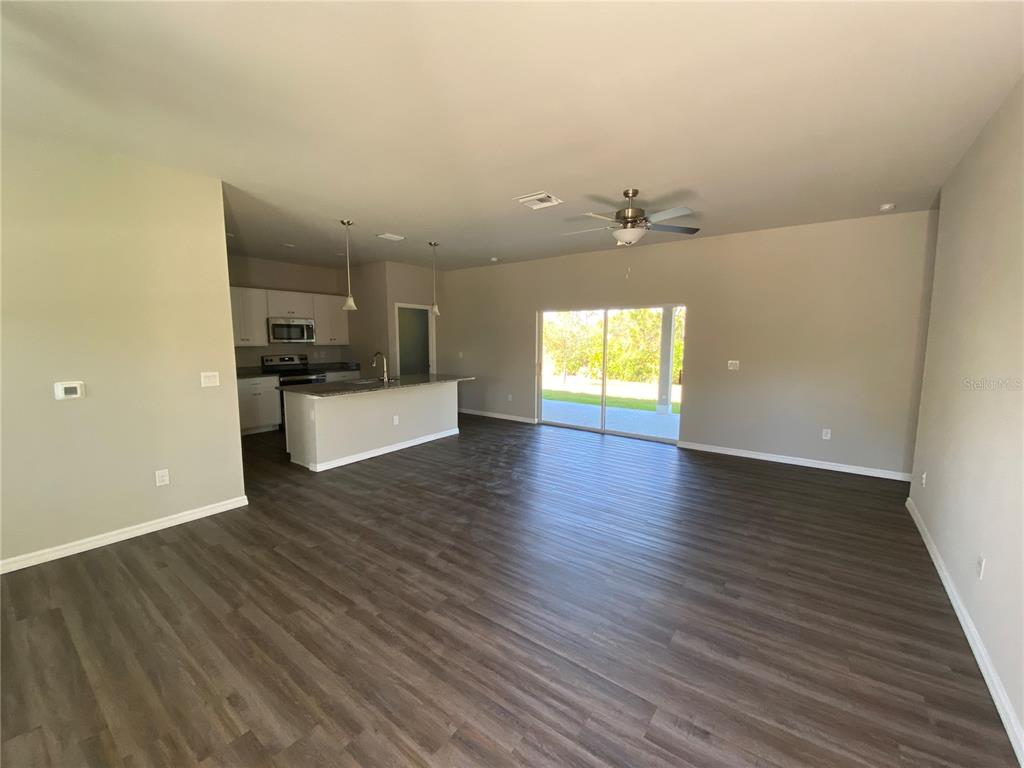 An open-concept living area features dark wood-look flooring, a kitchen with white cabinets, and sliding doors — 5625 ABELMAN ROAD, NORTH PORT, FL