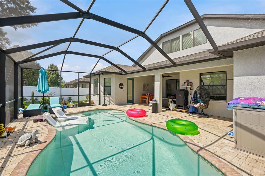 A screened-in patio features a swimming pool with lounge chairs and colorful pool floats — 652 TIERRA DRIVE, SPRING HILL, FL