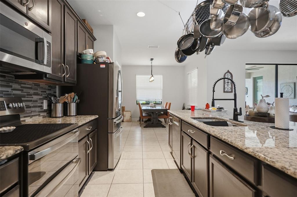 A kitchen features dark wood cabinets, granite countertops, stainless steel appliances, and a hanging pot rack — 652 TIERRA DRIVE, SPRING HILL, FL