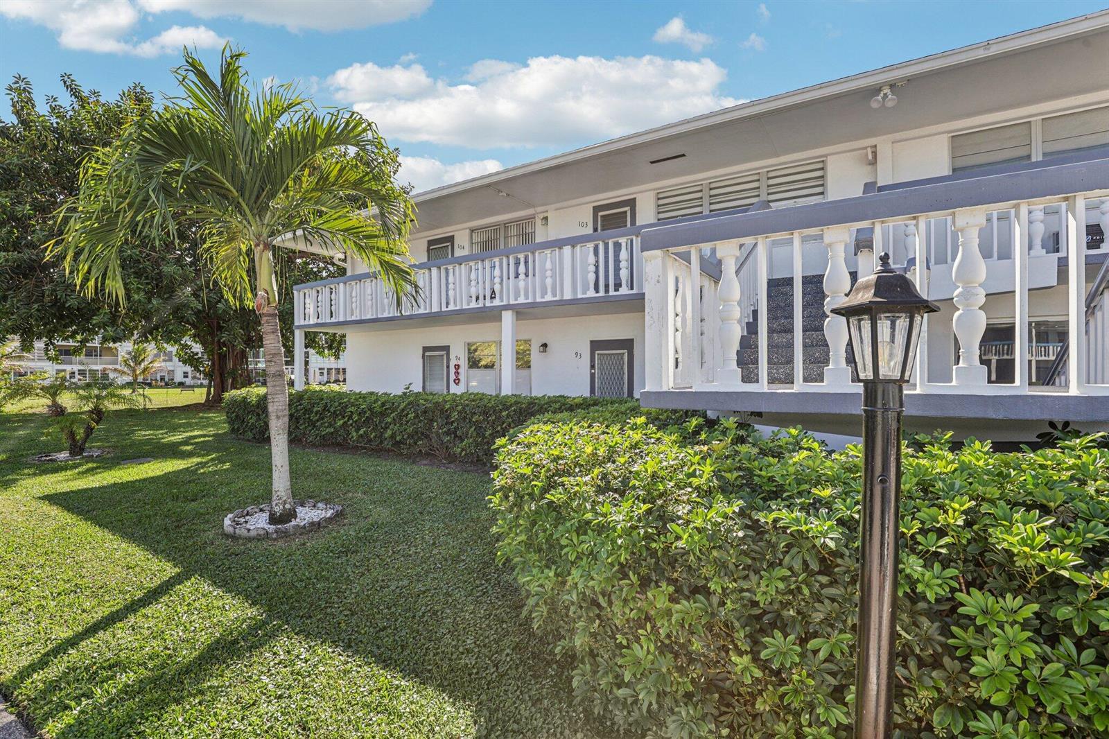 A two-story apartment building with a white balcony, palm tree, and manicured landscaping — 104 Oakridge # H, Deerfield Beach FL 33442, DEERFIELD BEACH, FL