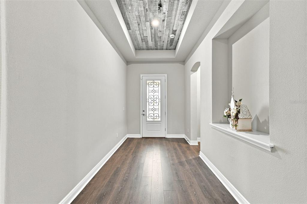 A bright entryway features wood-look flooring, a white front door, and a rustic wood-paneled ceiling — 5335 SILVER SUN DRIVE, APOLLO BEACH, FL