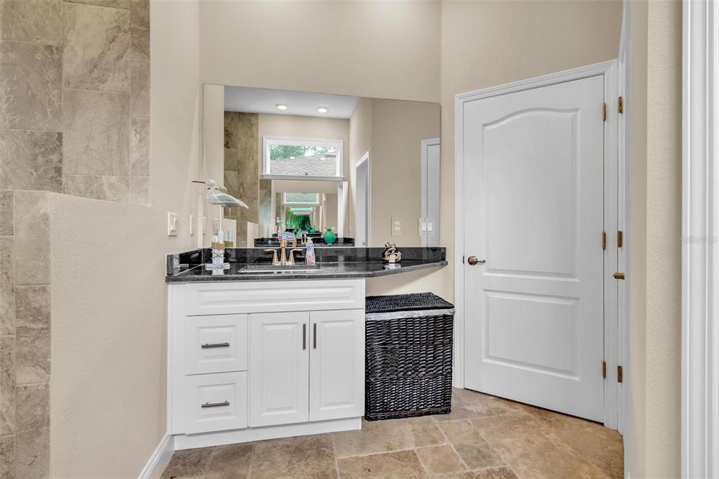 A bathroom vanity with a dark granite countertop, white cabinets, and a large wall mirror — 10 POINT OF WOODS DRIVE, PALM COAST, FL