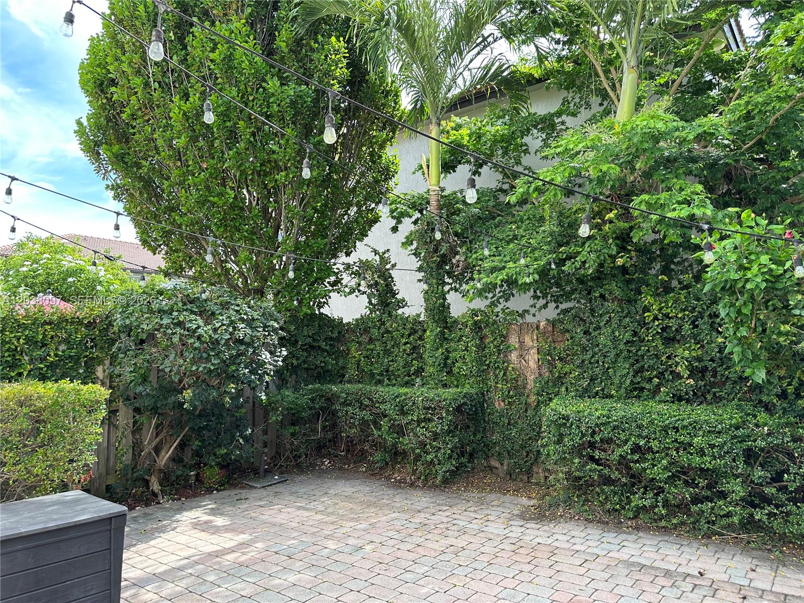 A paved patio area features string lights hanging above lush green trees and shrubs — 2555 SW 147th Path # 2555, Miami FL 33185, MIAMI, FL