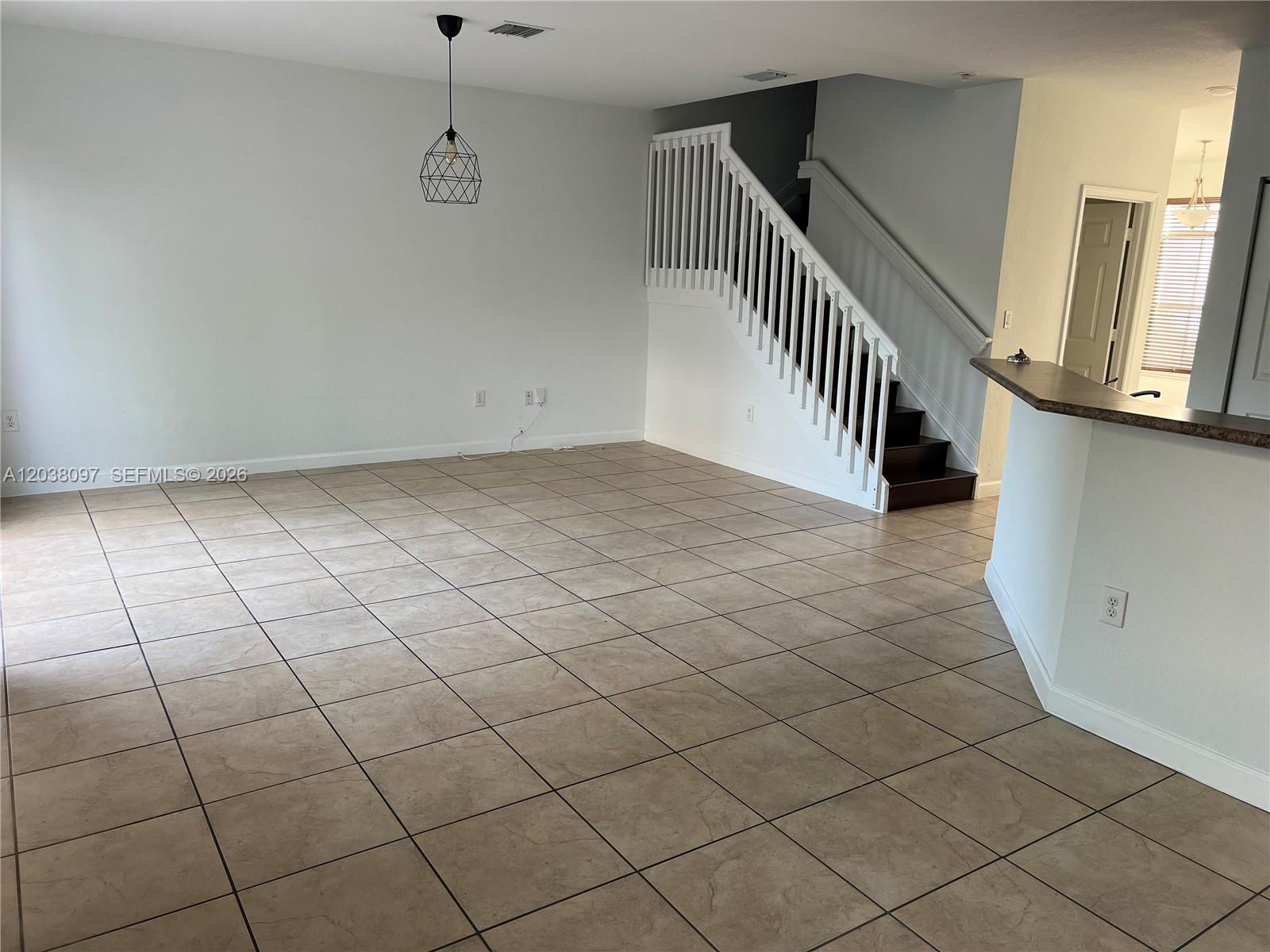 An open living area features large beige floor tiles, a staircase, and a pendant light — 2555 SW 147th Path # 2555, Miami FL 33185, MIAMI, FL