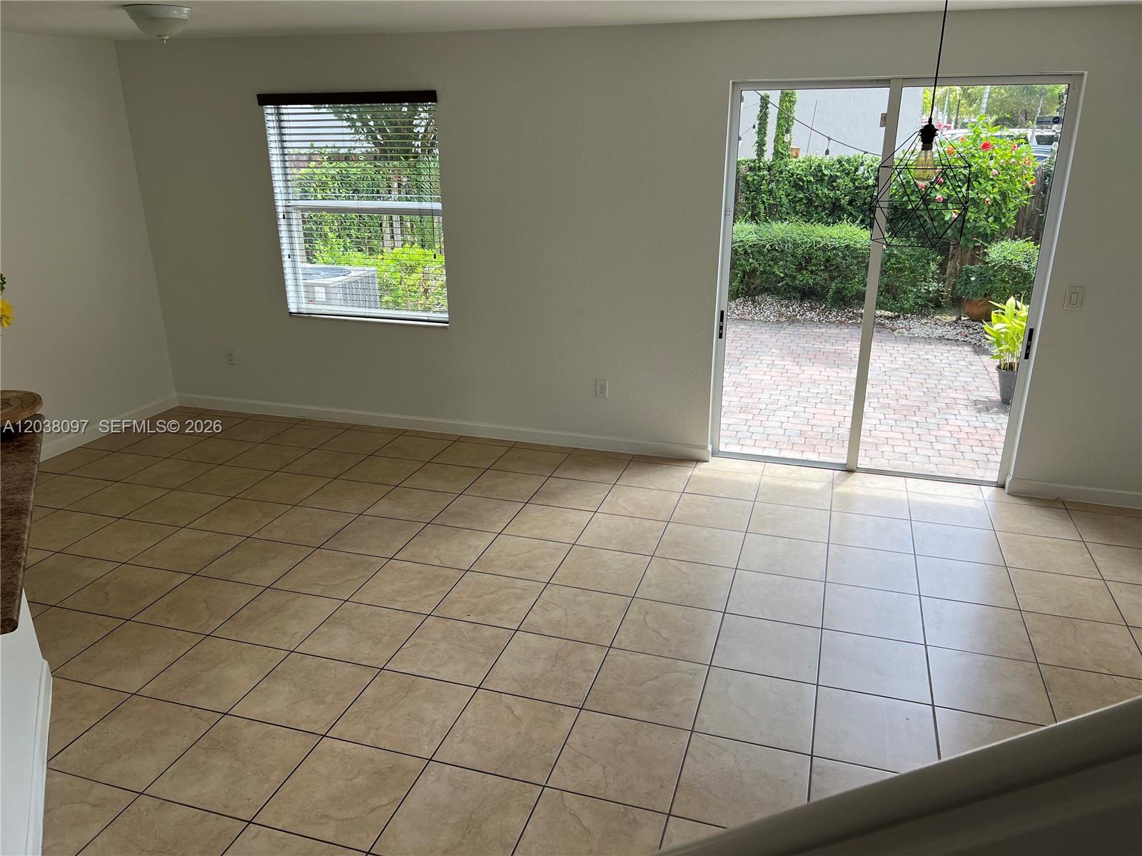An empty room features beige tile flooring, a window with blinds, and a sliding glass door — 2555 SW 147th Path # 2555, Miami FL 33185, MIAMI, FL