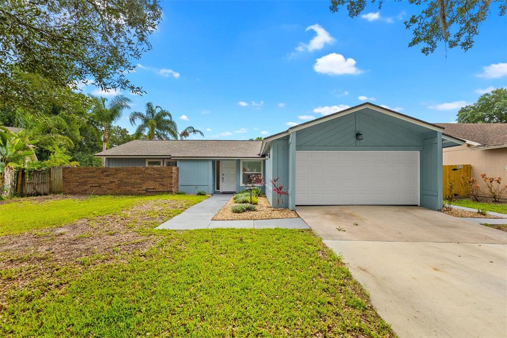 A single-story house with blue siding, a white garage door, and a brick wall — 15917 COUNTRY FARM PLACE, TAMPA, FL