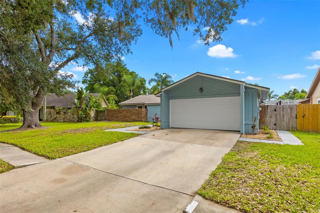 A blue house with a white garage door and a concrete driveway under a tree — 15917 COUNTRY FARM PLACE, TAMPA, FL