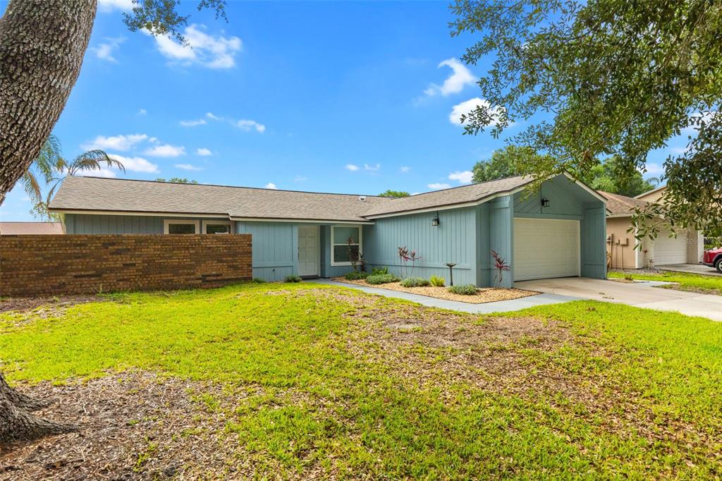 A single-story blue house with a brick wall, a garage, and a front lawn — 15917 COUNTRY FARM PLACE, TAMPA, FL