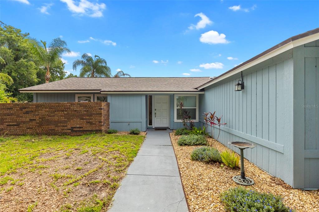 A blue house with vertical siding, a brick wall, and a concrete walkway to the entrance — 15917 COUNTRY FARM PLACE, TAMPA, FL