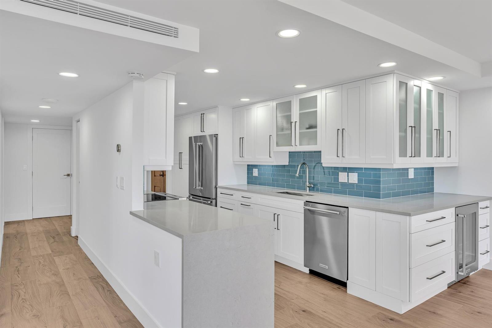 A modern kitchen features white cabinetry, a blue subway tile backsplash, and stainless steel appliances — 2175 S Ocean Boulevard # 305, Delray Beach FL 33483, DELRAY BEACH, FL