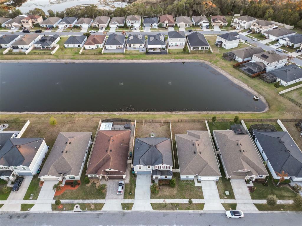 An aerial view shows a suburban neighborhood with houses bordering a large retention pond — 13916 RUSHING CREEK RUN, ORLANDO, FL
