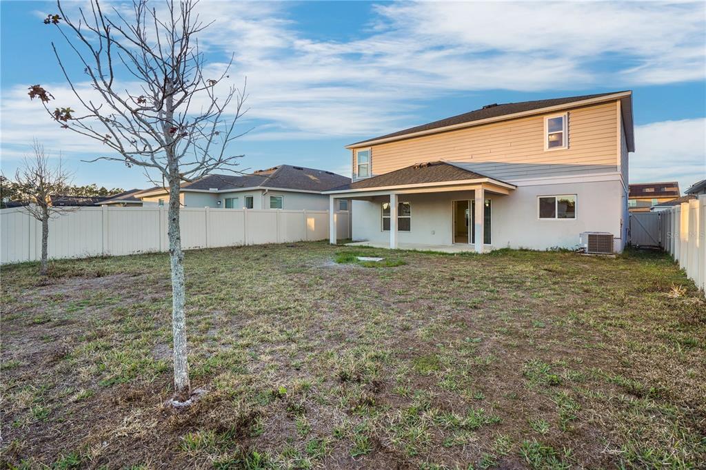The backyard of a two-story house features a covered patio, vinyl fencing, and sparse grass — 13916 RUSHING CREEK RUN, ORLANDO, FL