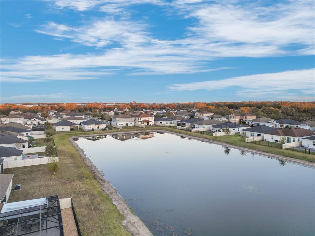 An aerial view shows a suburban neighborhood with houses surrounding a central retention pond — 13916 RUSHING CREEK RUN, ORLANDO, FL