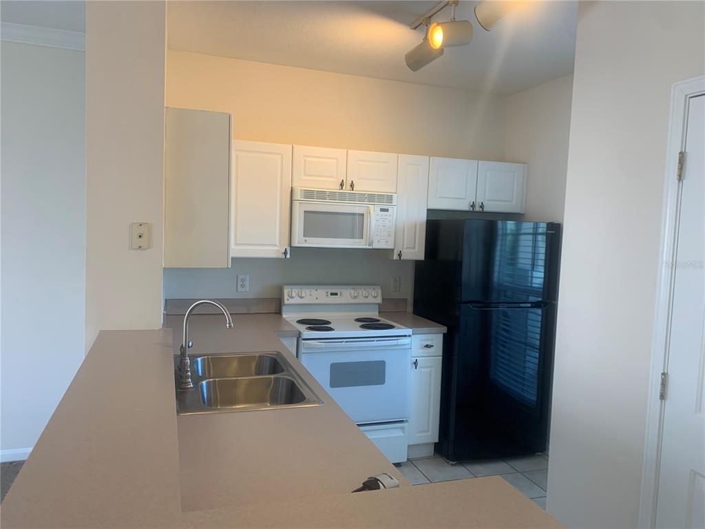A kitchen features white cabinets, white appliances, a black refrigerator, and a double-basin sink — 573 WATER STREET UNIT 573, CELEBRATION, FL
