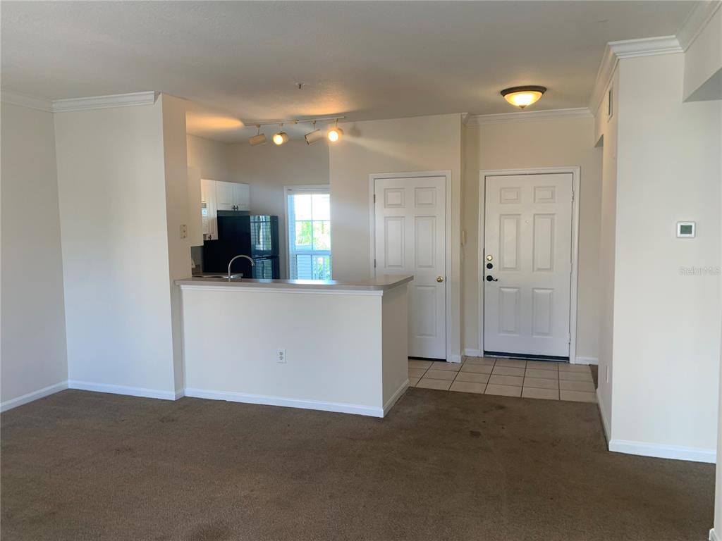 A living room with beige carpet opens to a kitchen with a breakfast bar — 573 WATER STREET UNIT 573, CELEBRATION, FL