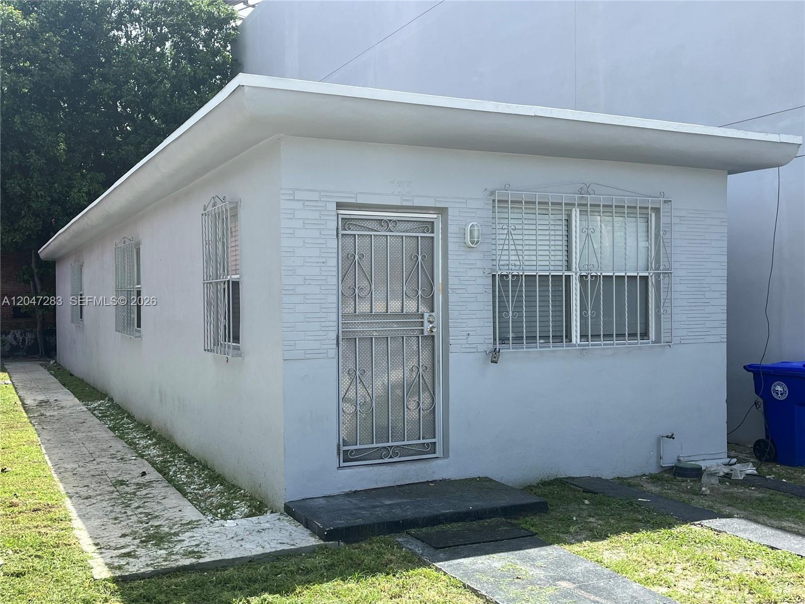A small, light-gray, single-story house features a metal security door and window bars — 733 NW 4th Ave, Miami FL 33136, MIAMI, FL