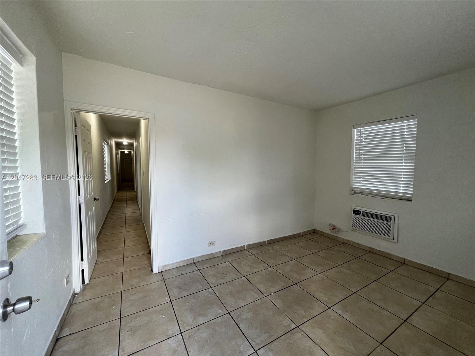 An empty room features white walls, tan tile flooring, a window, and a wall-mounted air conditioner — 733 NW 4th Ave, Miami FL 33136, MIAMI, FL