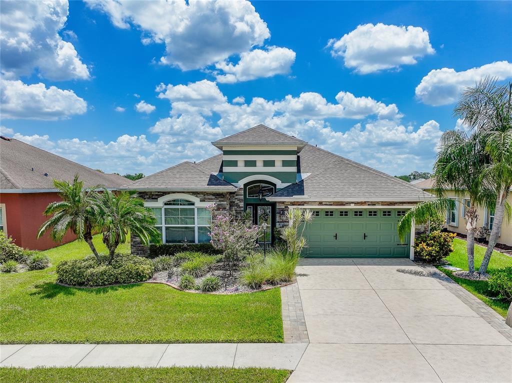 A single-story house features a green garage, stone facade, and a landscaped front yard — 7830 113TH AVENUE E, PARRISH, FL