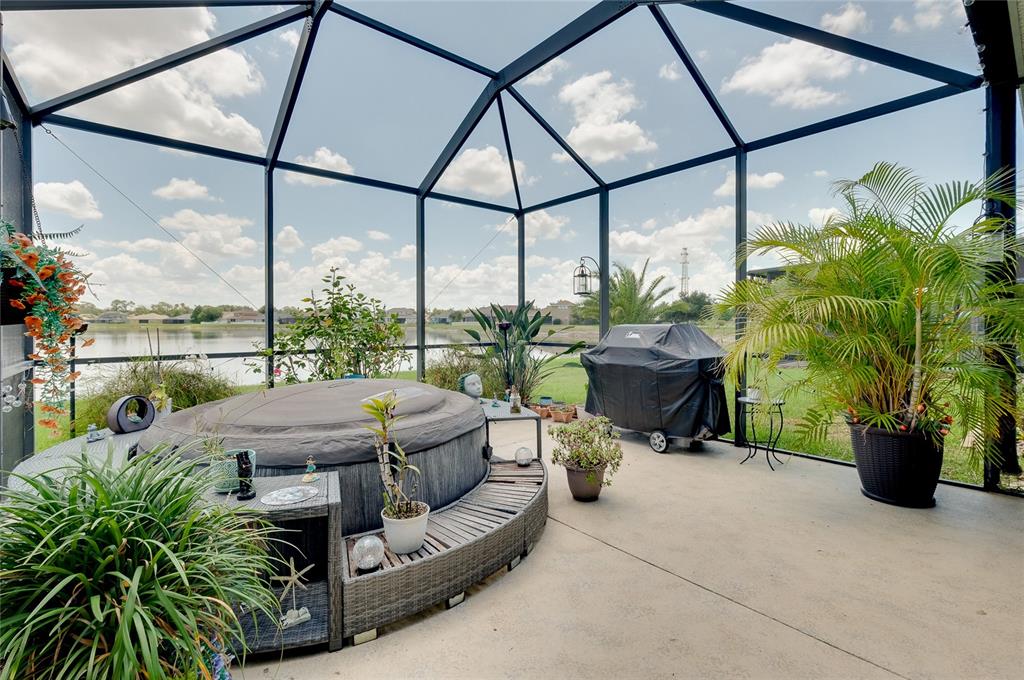 A screened-in patio features a hot tub, a covered grill, and potted plants overlooking water — 7830 113TH AVENUE E, PARRISH, FL