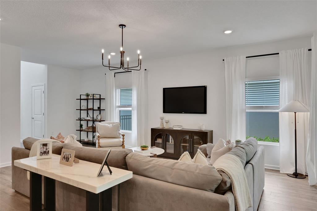 A living room features a sectional sofa, a television, a chandelier, and two windows — 5716 LAGOON CRUISE WAY, JACKSONVILLE, FL