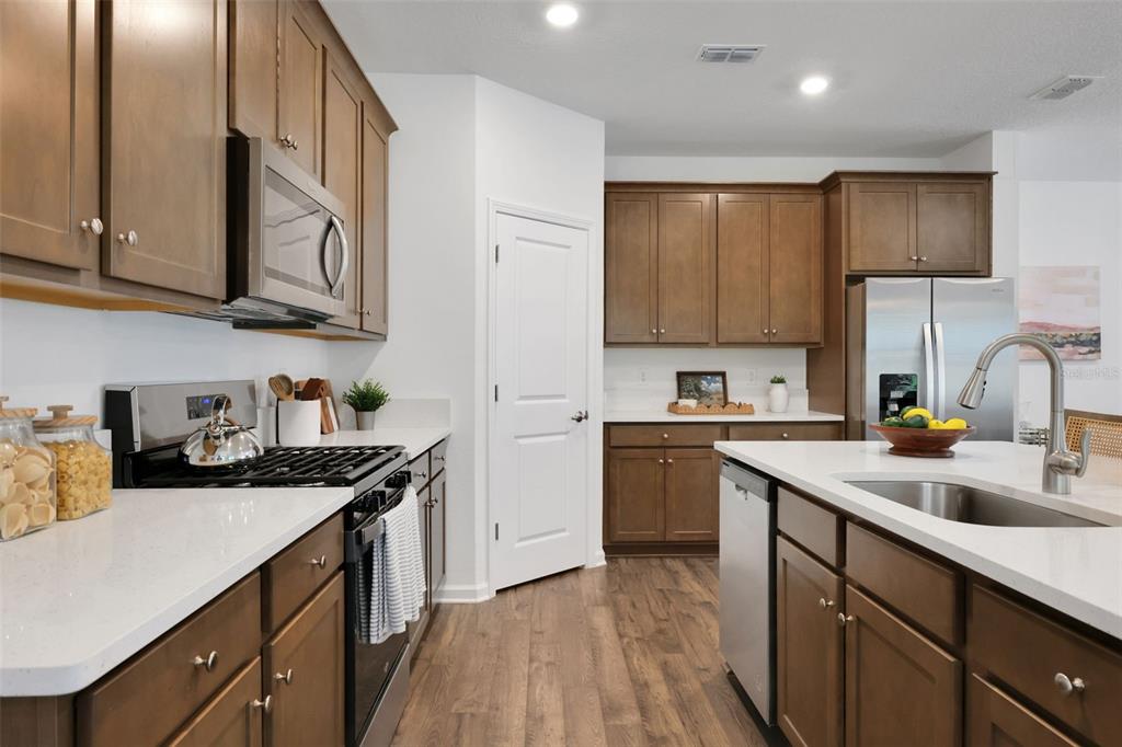 A kitchen features brown wooden cabinets, white countertops, stainless steel appliances, and wood-look flooring — 5716 LAGOON CRUISE WAY, JACKSONVILLE, FL