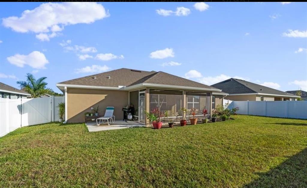 A backyard view of a house with a screened-in patio and a white vinyl fence — 8516 WATERSTONE BOULEVARD, FORT PIERCE, FL