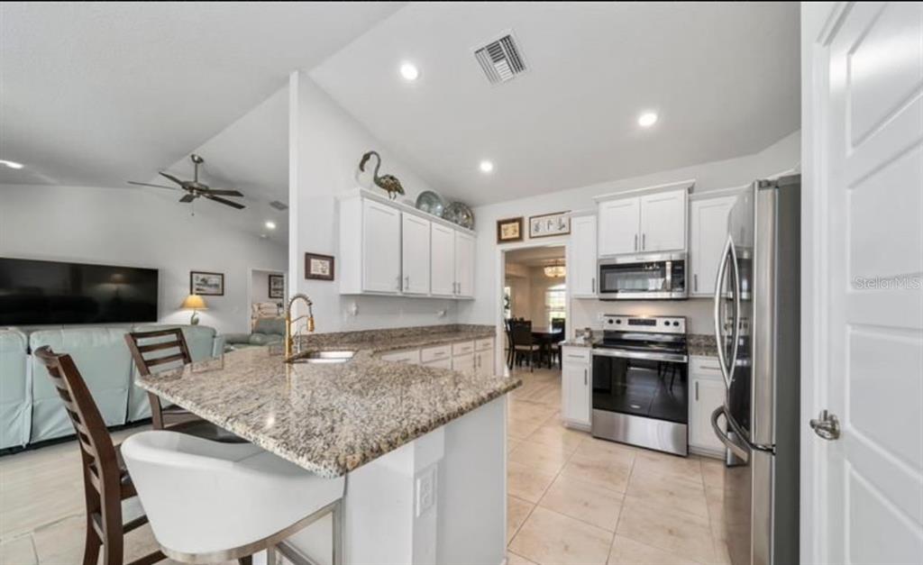 A kitchen with granite countertops, white cabinets, stainless steel appliances, and a breakfast bar — 8516 WATERSTONE BOULEVARD, FORT PIERCE, FL