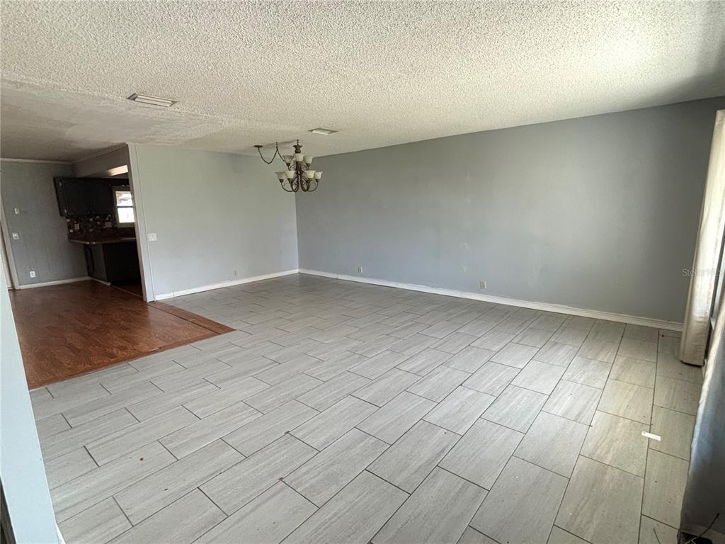 A spacious room features gray tile flooring, a light gray wall, and a hanging chandelier — 212 OVERLOOK DRIVE, WINTER HAVEN, FL