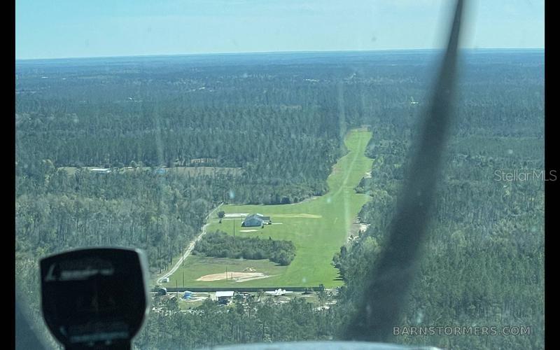 An aerial view shows a private grass airstrip surrounded by dense forest and a house — 22303 NW LONGLEAF ROAD, FOUNTAIN, FL