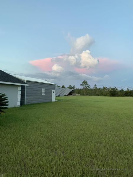 A gray metal building stands next to a house overlooking a large, grassy field — 22303 NW LONGLEAF ROAD, FOUNTAIN, FL