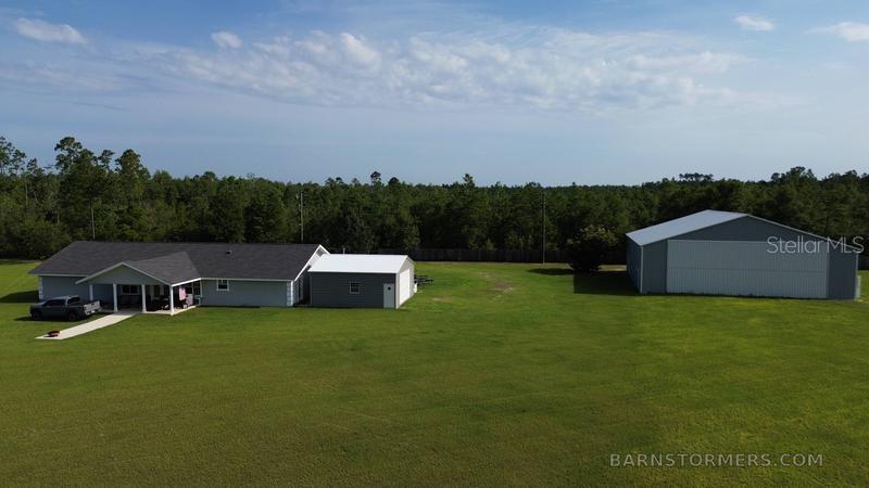An aerial view shows a house, a detached garage, and a large hangar on grass — 22303 NW LONGLEAF ROAD, FOUNTAIN, FL